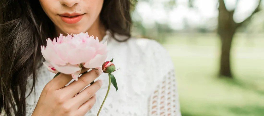 Naine_nuusutamas_õrnroosat_pojengi_kuidas-menopausi-ajal--nagu-lill-õitsele-puhkede-ja-millised-taimed-aitavad-menopausi-sümptomeid-leevendada